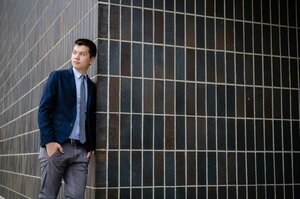 Reed Oei stands near a black tiled wall. 