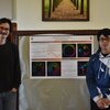 Two students stand in front of their research poster. The poster contains colorful fractal patterns on a black background. 