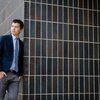 Reed Oei stands near a black tiled wall. 