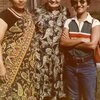 Three women pose for a photo. The woman on the left is wearing a black blouse and colorful sari. The woman in the middle is wearing a paisley print dress. The woman on the right is wearing a striped polo shirt, blue jean, and sunglasses. 